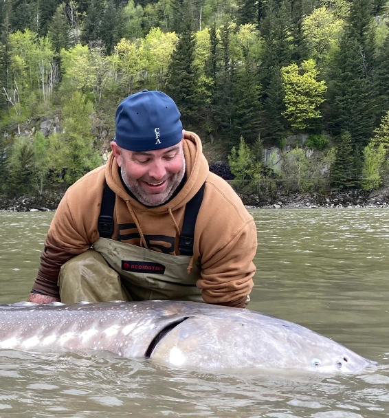 a man next to a big sturgeon in the fraser river