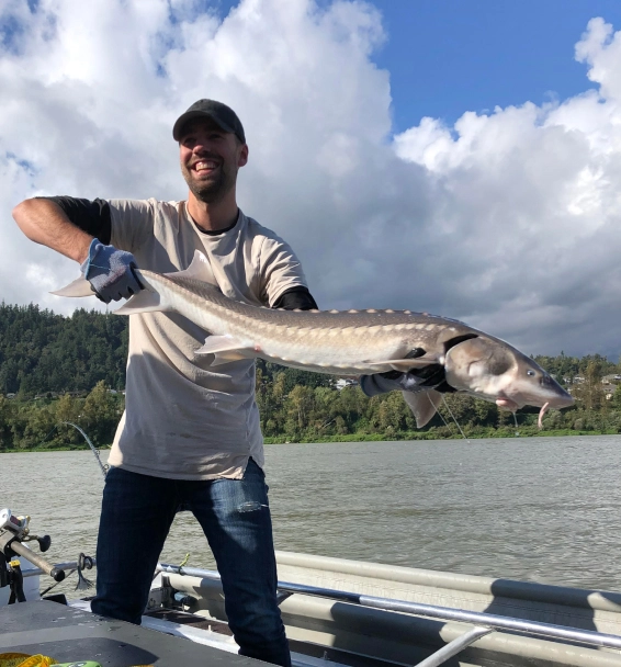 Man holding a large white sturgeon on a fishing boat during a guided Fraser River fishing trip