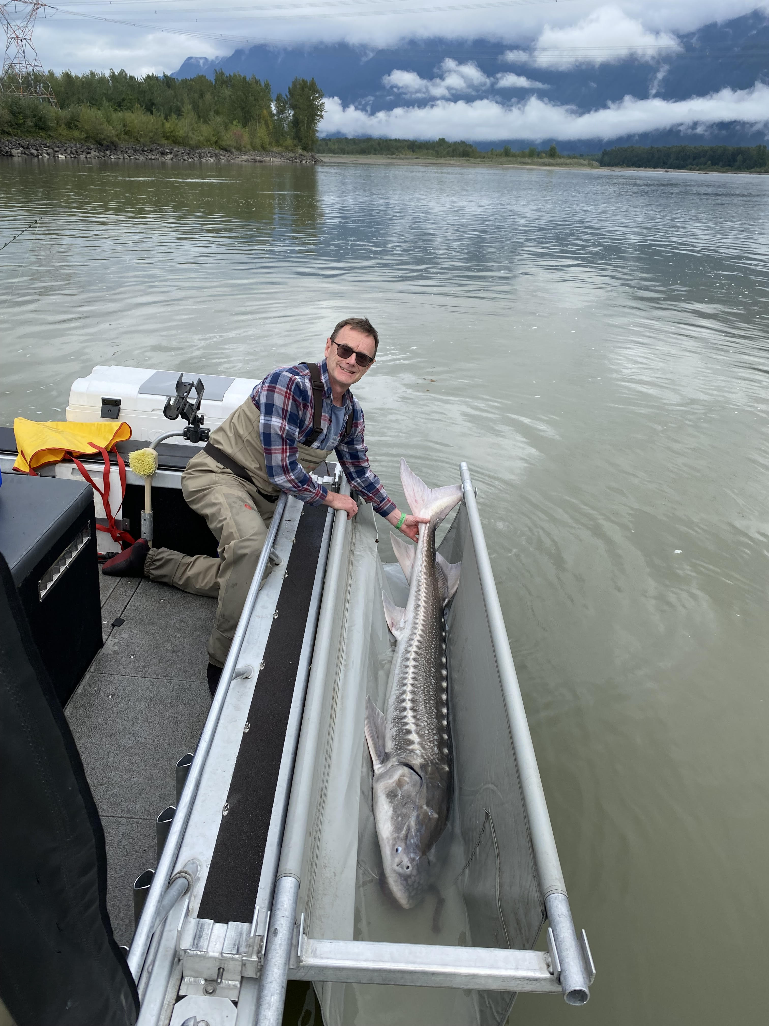 a man next to a 5 feet sturgeon on a boat